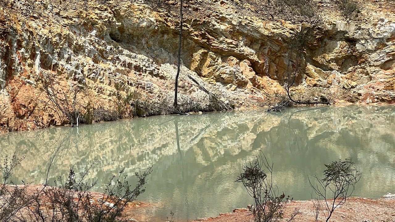 Abandoned open-pit mine with rust-coloured rock walls and a still water pool, reflecting the end of a mining operation. This illustrates end of mining in Emmaville in 1980s.