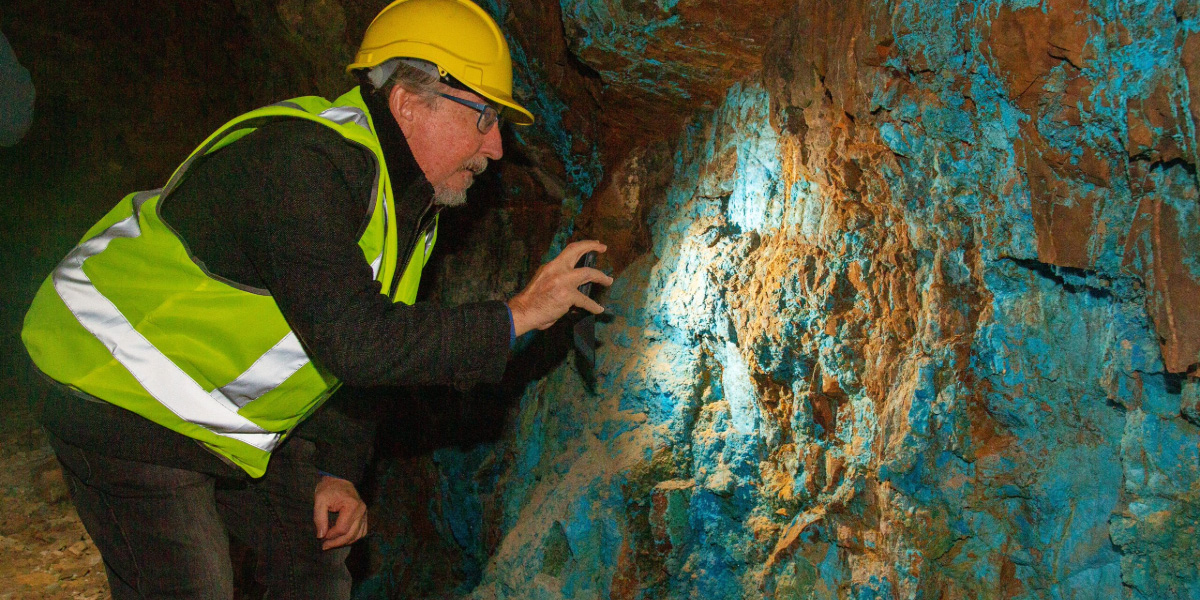 A geologist in a high-vis vest and hard hat examining vibrant blue mineral deposits, illustrating First Tin Plc's acquisition of Taronga in 2022.